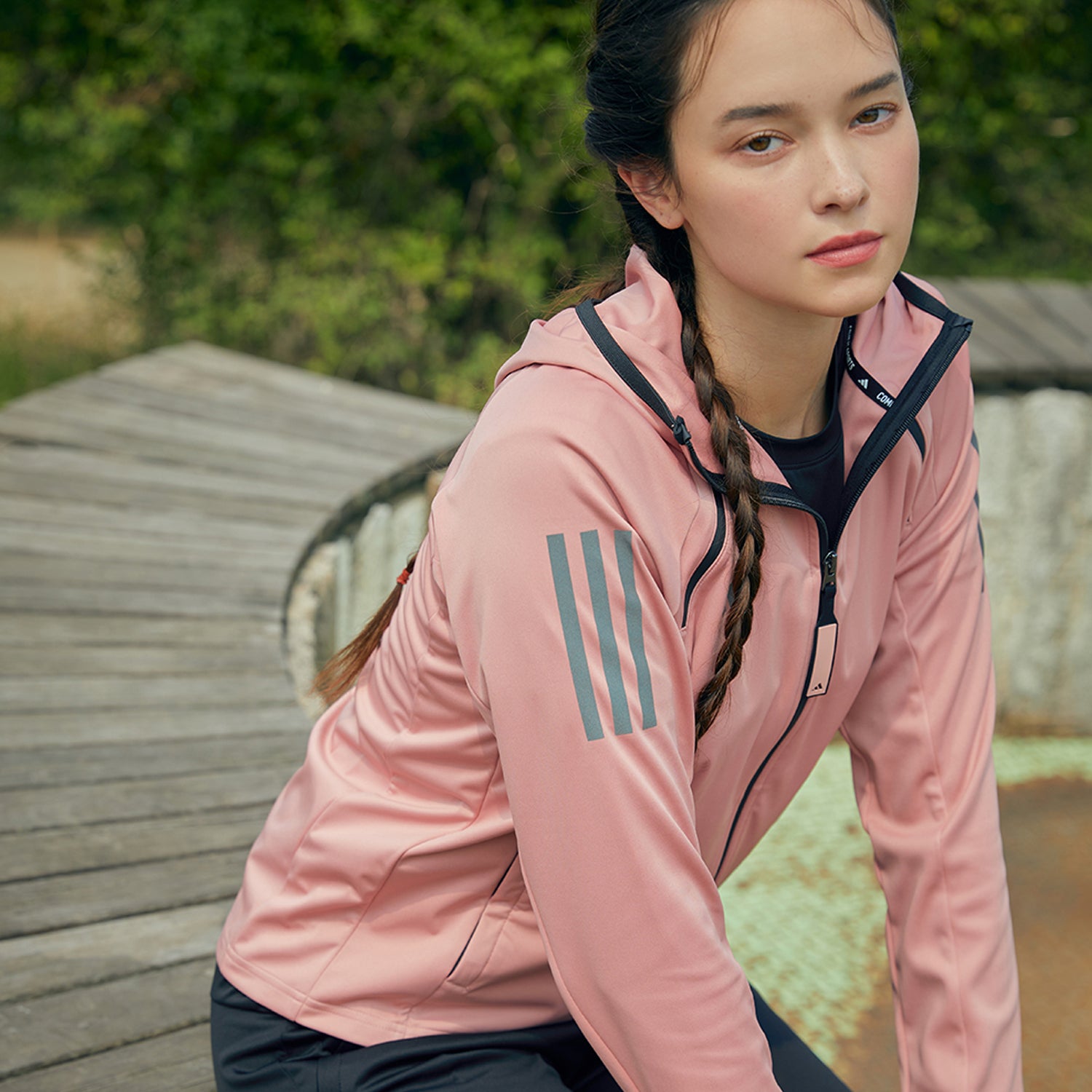 close up side view of woman in a park wearing a pink adidas athletic jacket