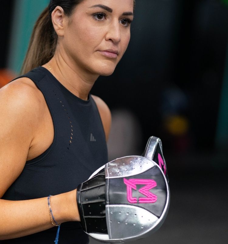 Woman wearing a black athletic outfit and boxing glove with a pink logo.