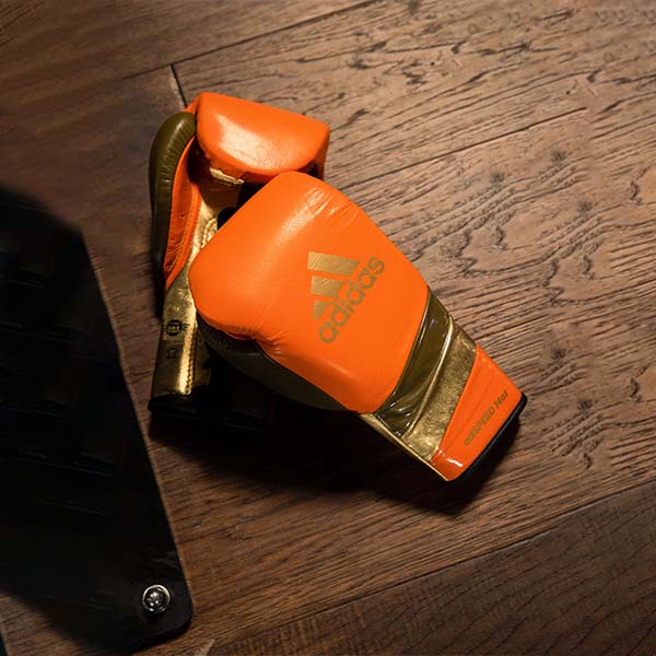 A pair of adiSPEED 500 PRO boxing gloves on a wooden surface.