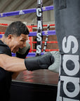 Man wearing Adidas boxing gloves punching a bag.