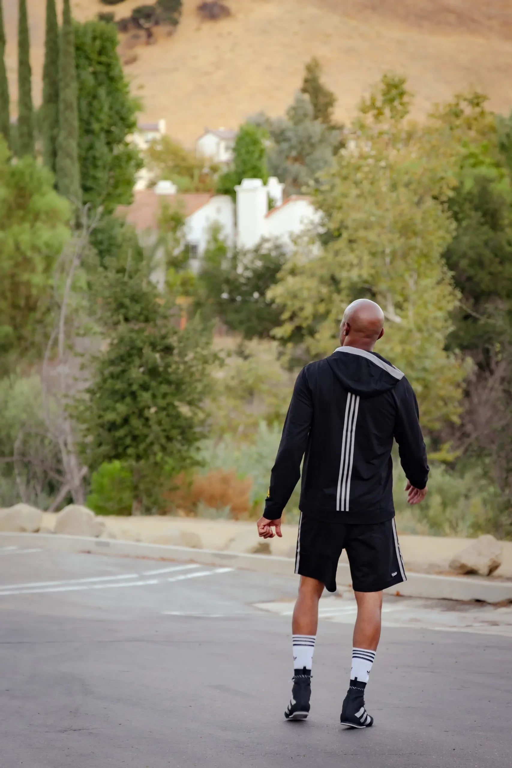 Man in black jacket and shorts walking in parking lot.