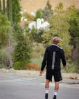 Man in black jacket and shorts walking in parking lot.