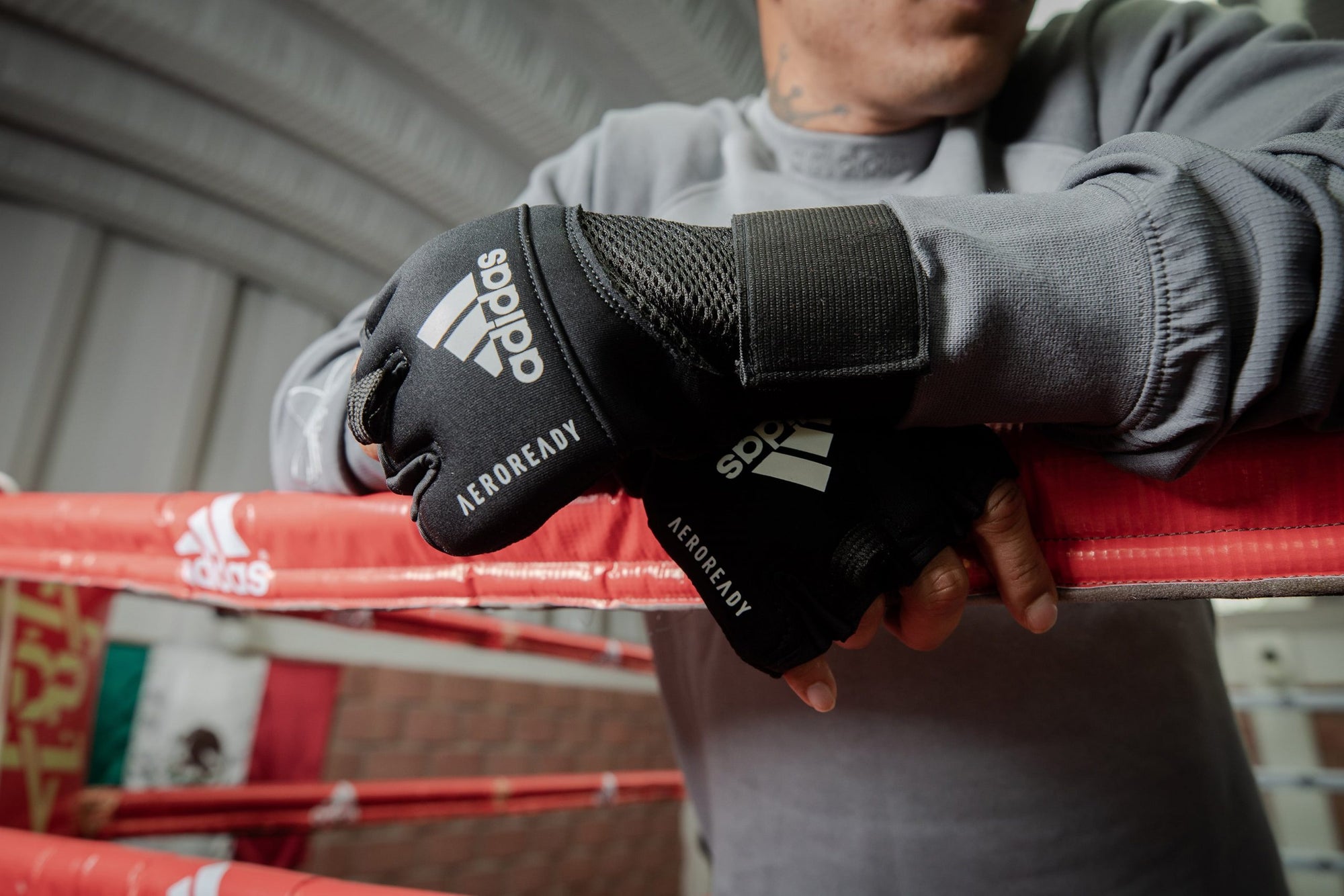 Person wearing gloves leaning on a boxing ring with Adidas wraps.