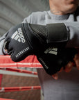 Person wearing gloves leaning on a boxing ring with Adidas wraps.