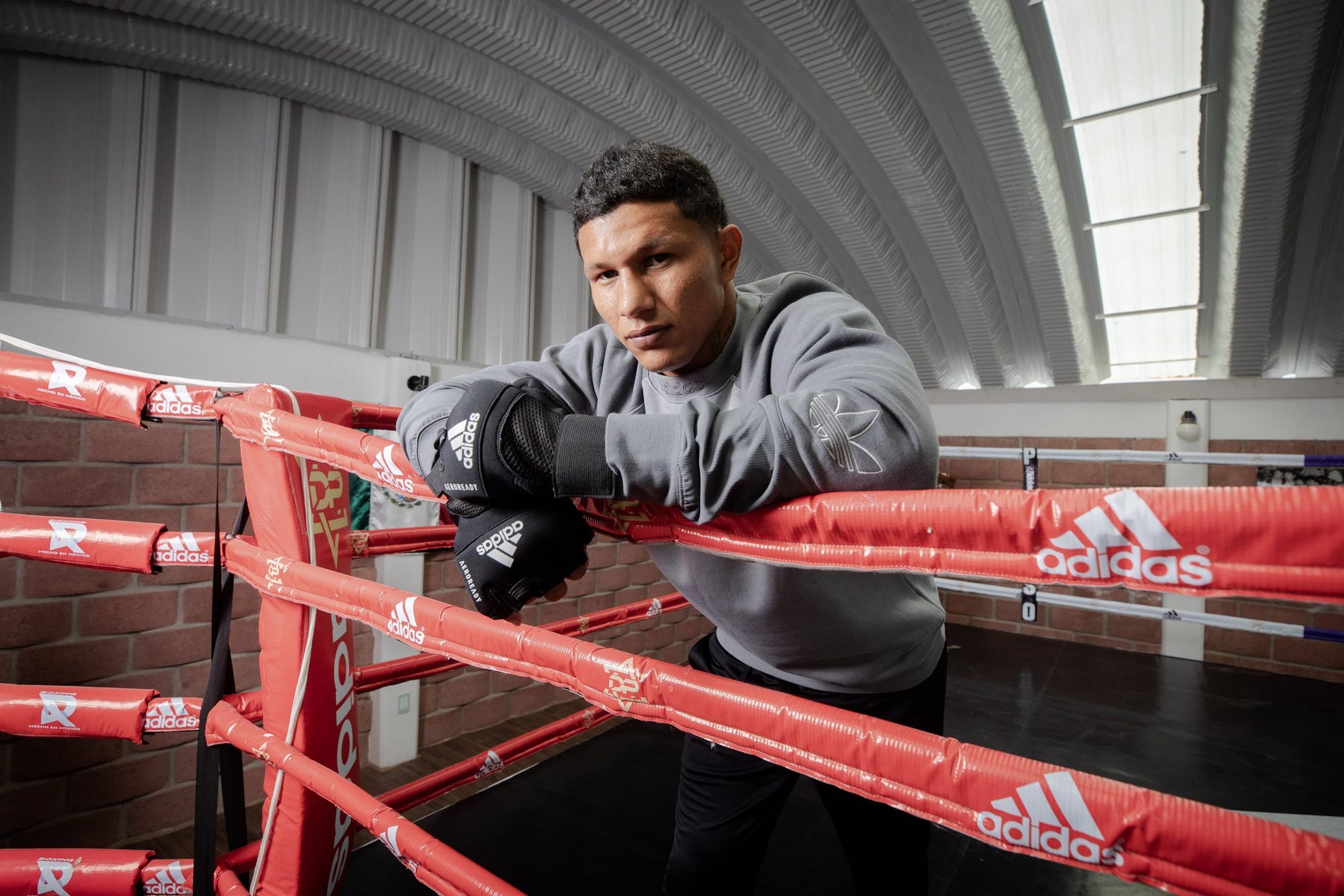 Man leaning on a boxing ring wearing Adidas gloves.