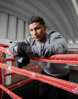 Man leaning on a boxing ring wearing Adidas gloves.