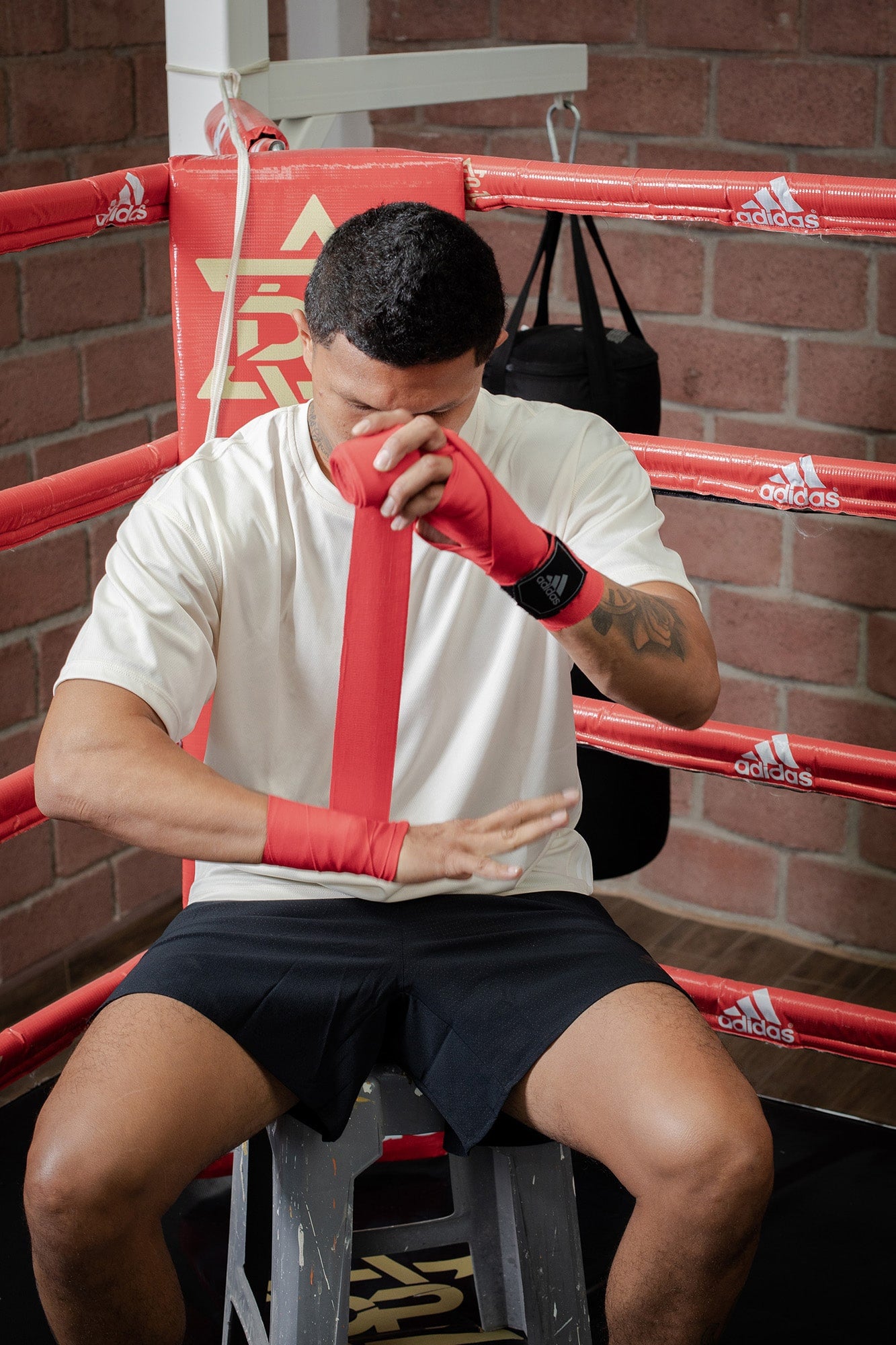 Man sitting in a boxing ring with hand wraps.