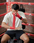 Man sitting in a boxing ring with hand wraps.