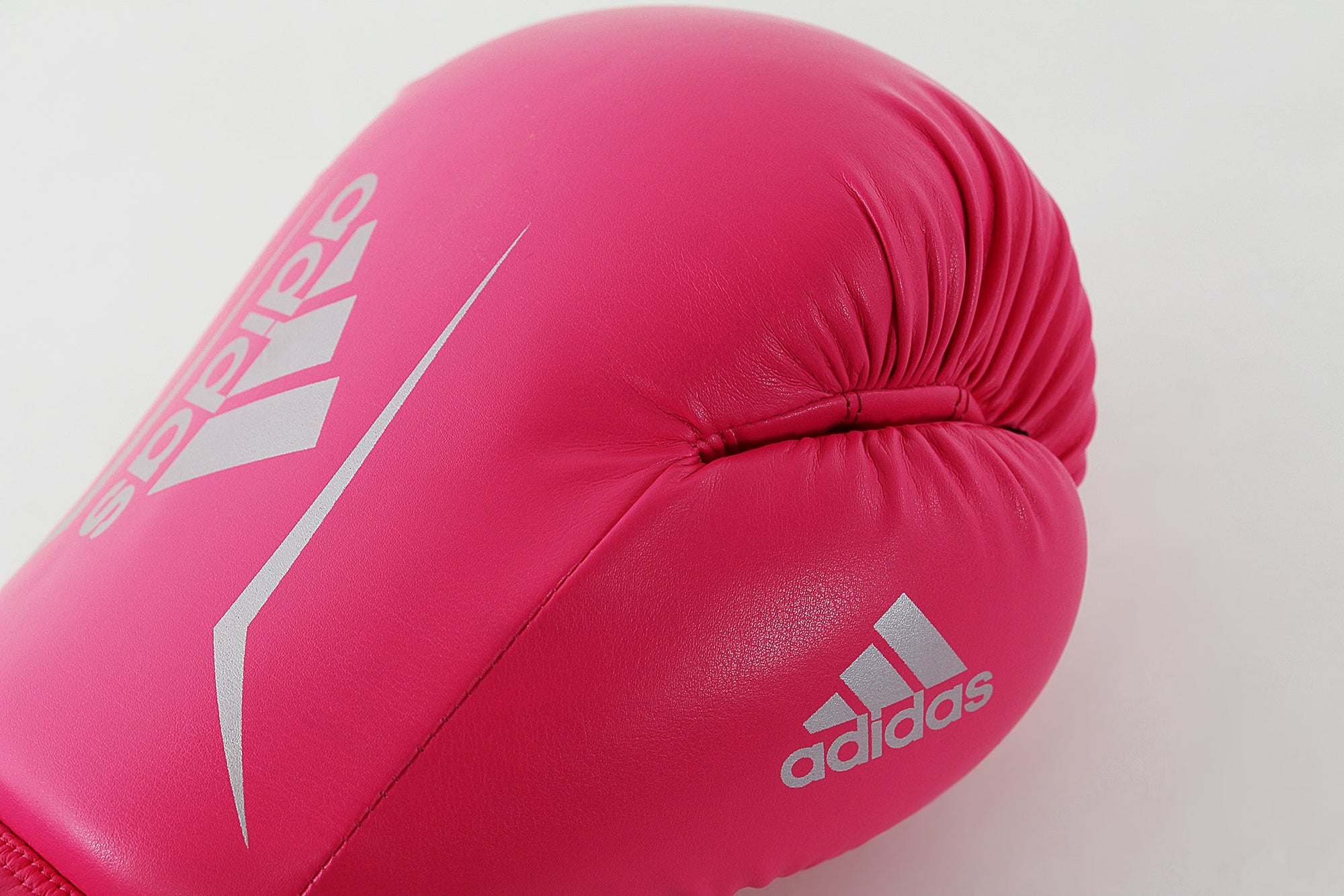 Pink boxing glove with silver adidas logo in close view.