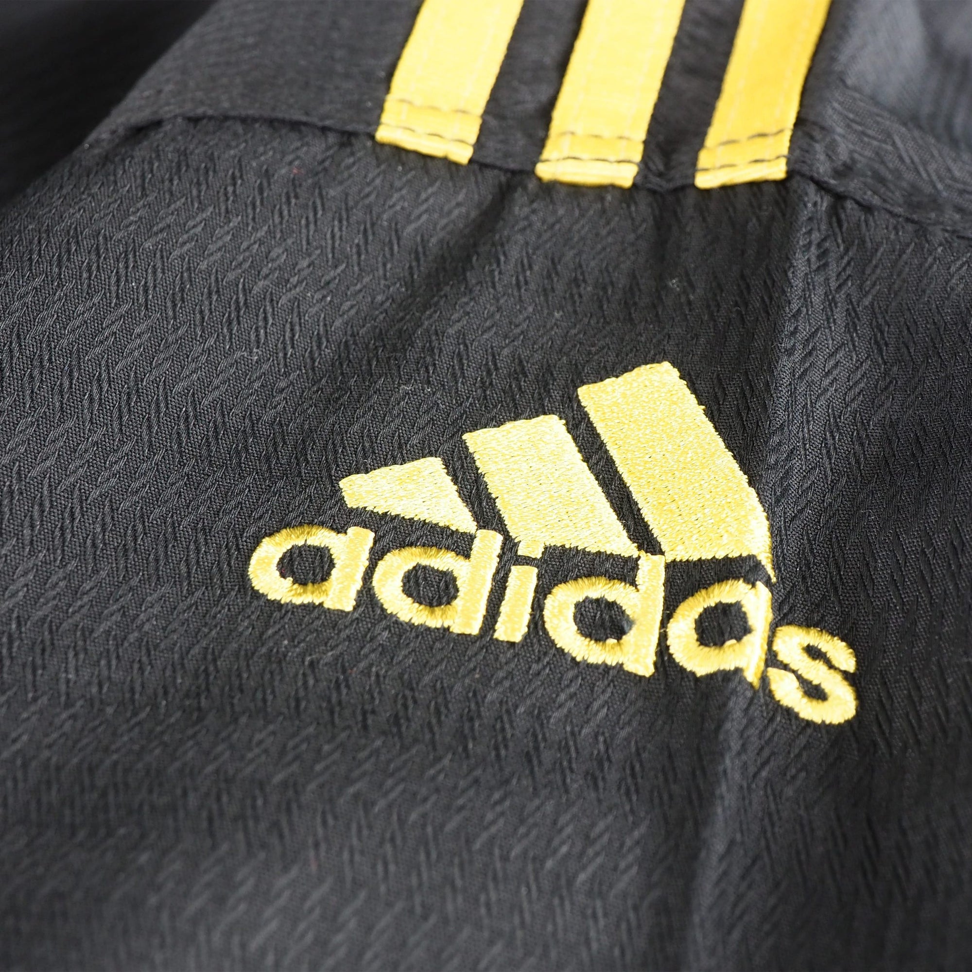 Close-up of black and yellow Adidas logo on uniform.