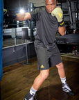 Man wearing boxing gloves in Adidas training shorts.