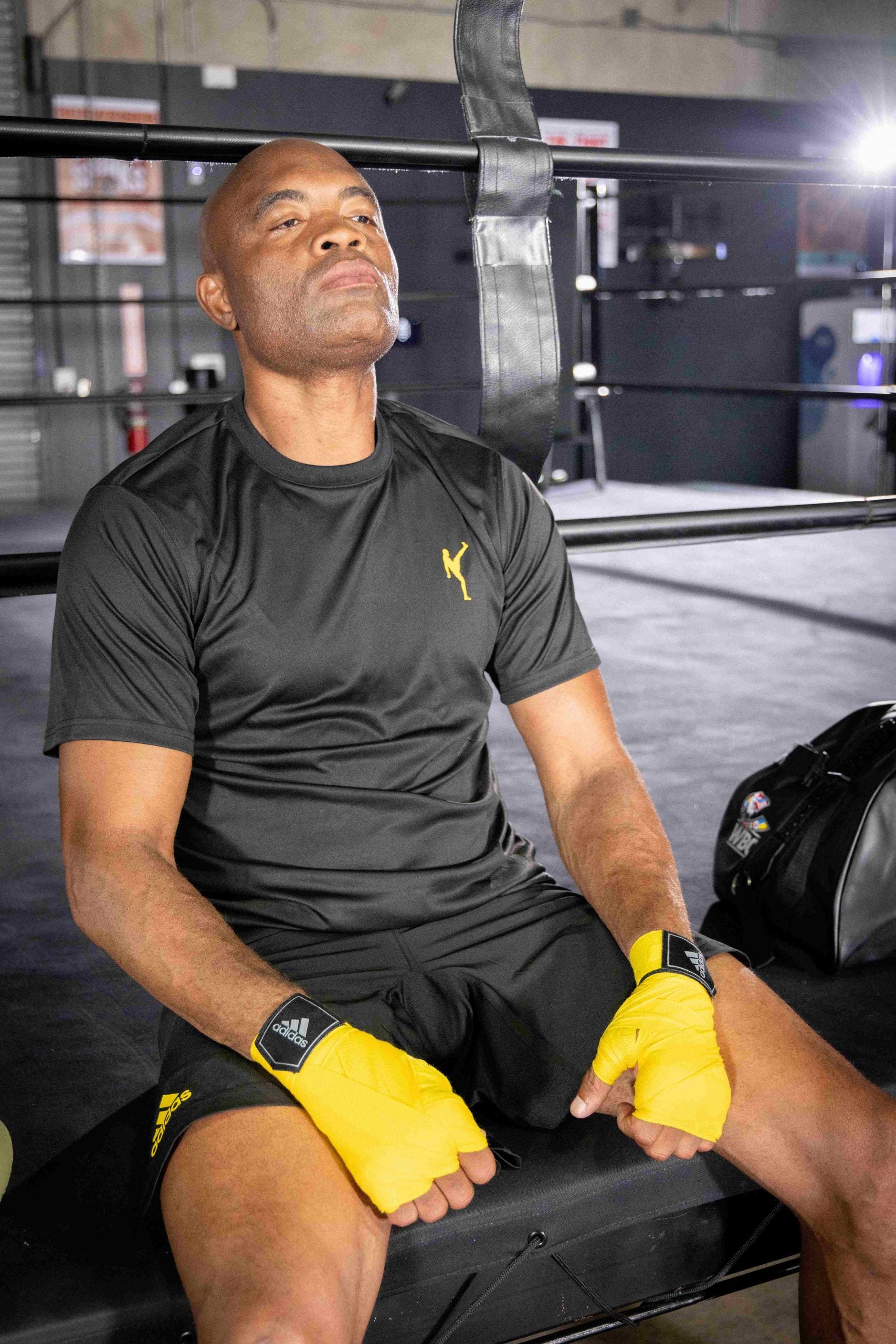 Man wearing yellow gloves sitting in a boxing ring.