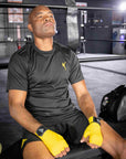 Man wearing yellow gloves sitting in a boxing ring.