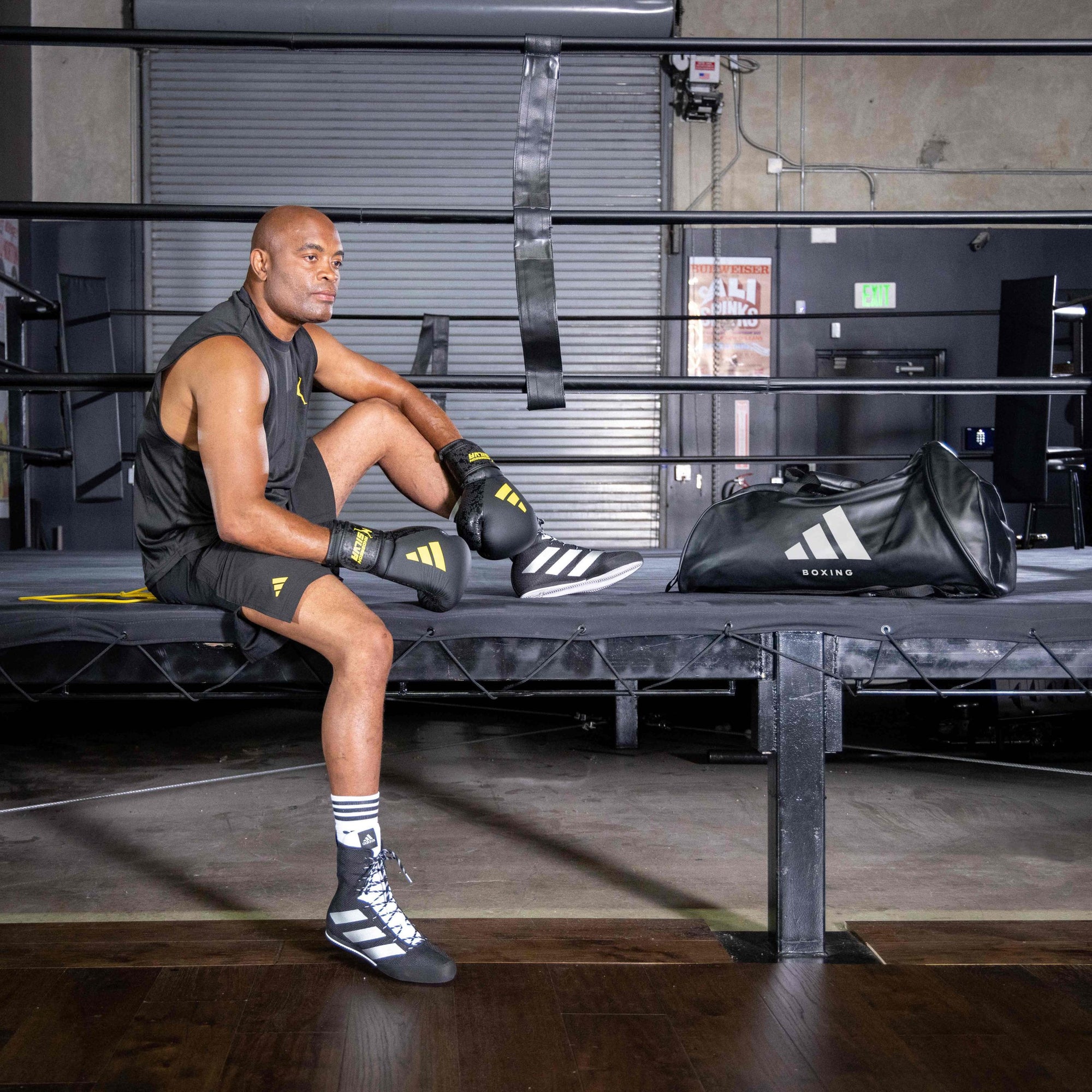 Man sitting on a bench in a boxing ring wearing gloves.