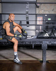 Man sitting on a bench in a boxing ring wearing gloves.