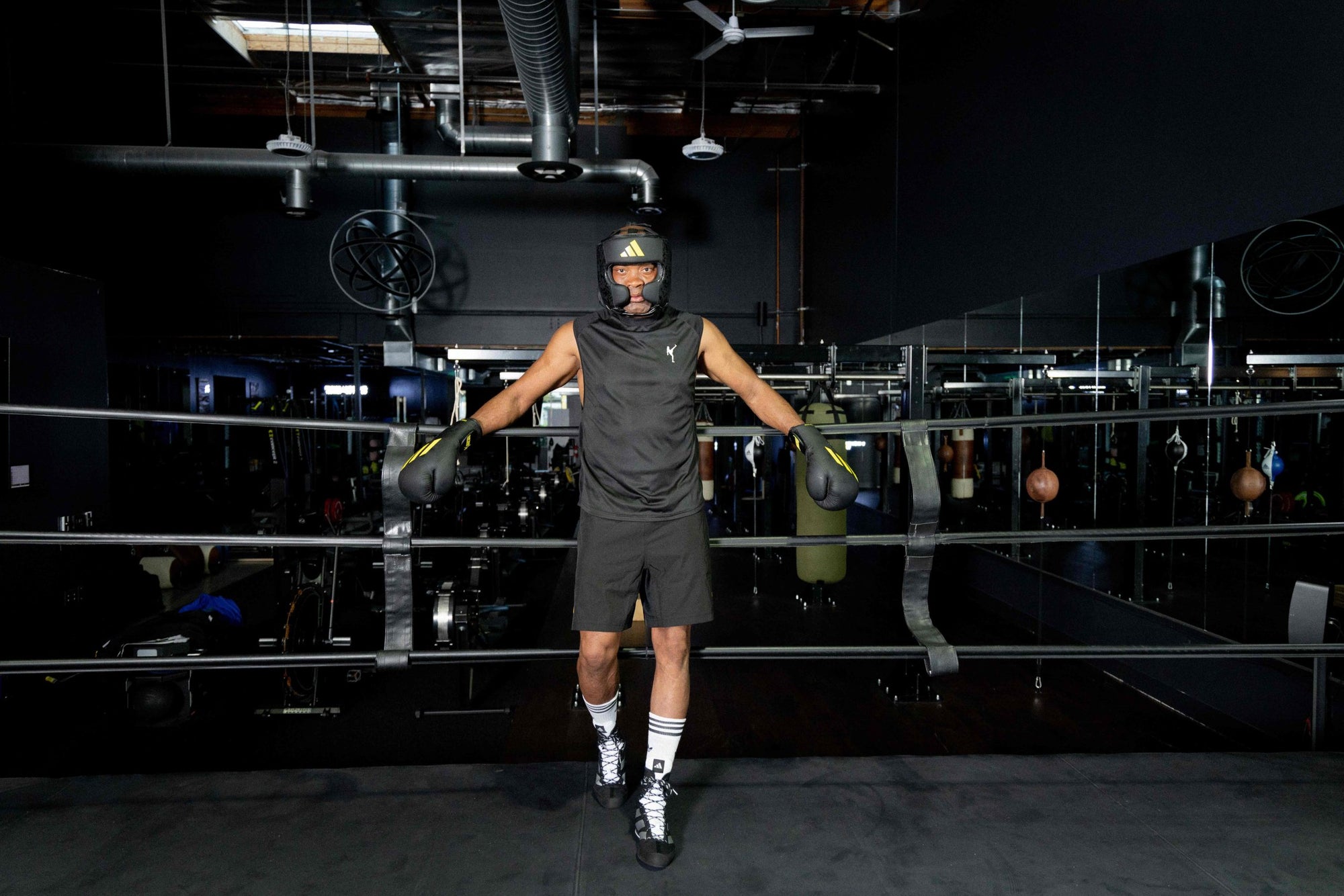 A man wearing boxing gloves and helmet stands in a boxing ring.