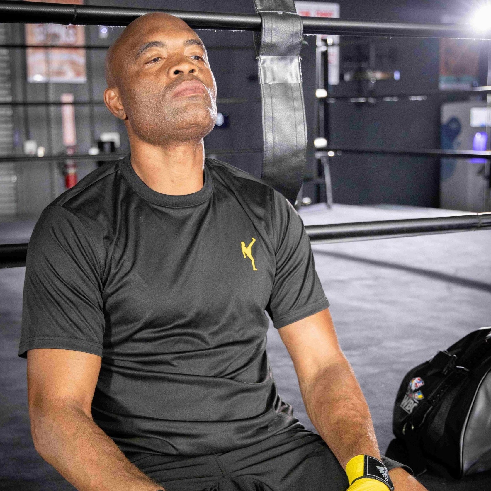 A man sitting in a boxing ring wearing a black XXL half sleeve T-shirt.