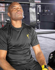 A man sitting in a boxing ring wearing a black XXL half sleeve T-shirt.