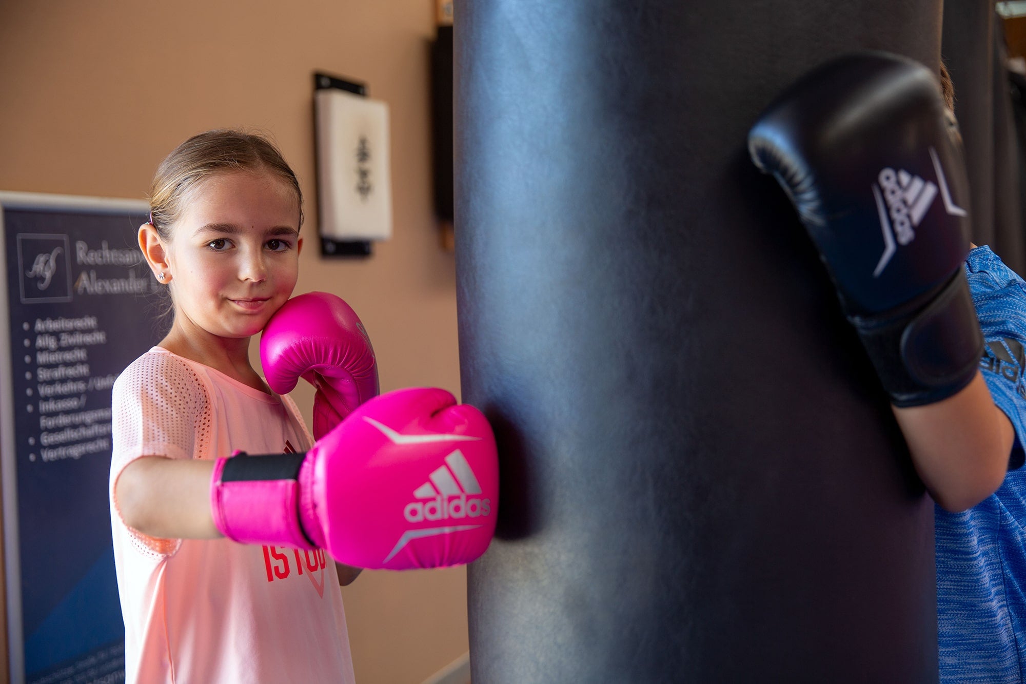 Girl wearing pink boxing gloves punching a bag.