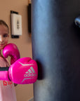 Girl wearing pink boxing gloves punching a bag.